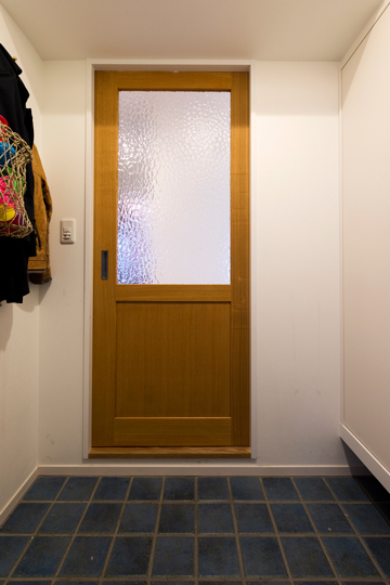 玄関の壁面に大容量の収納を造作。床には濃いブルー系のタイル