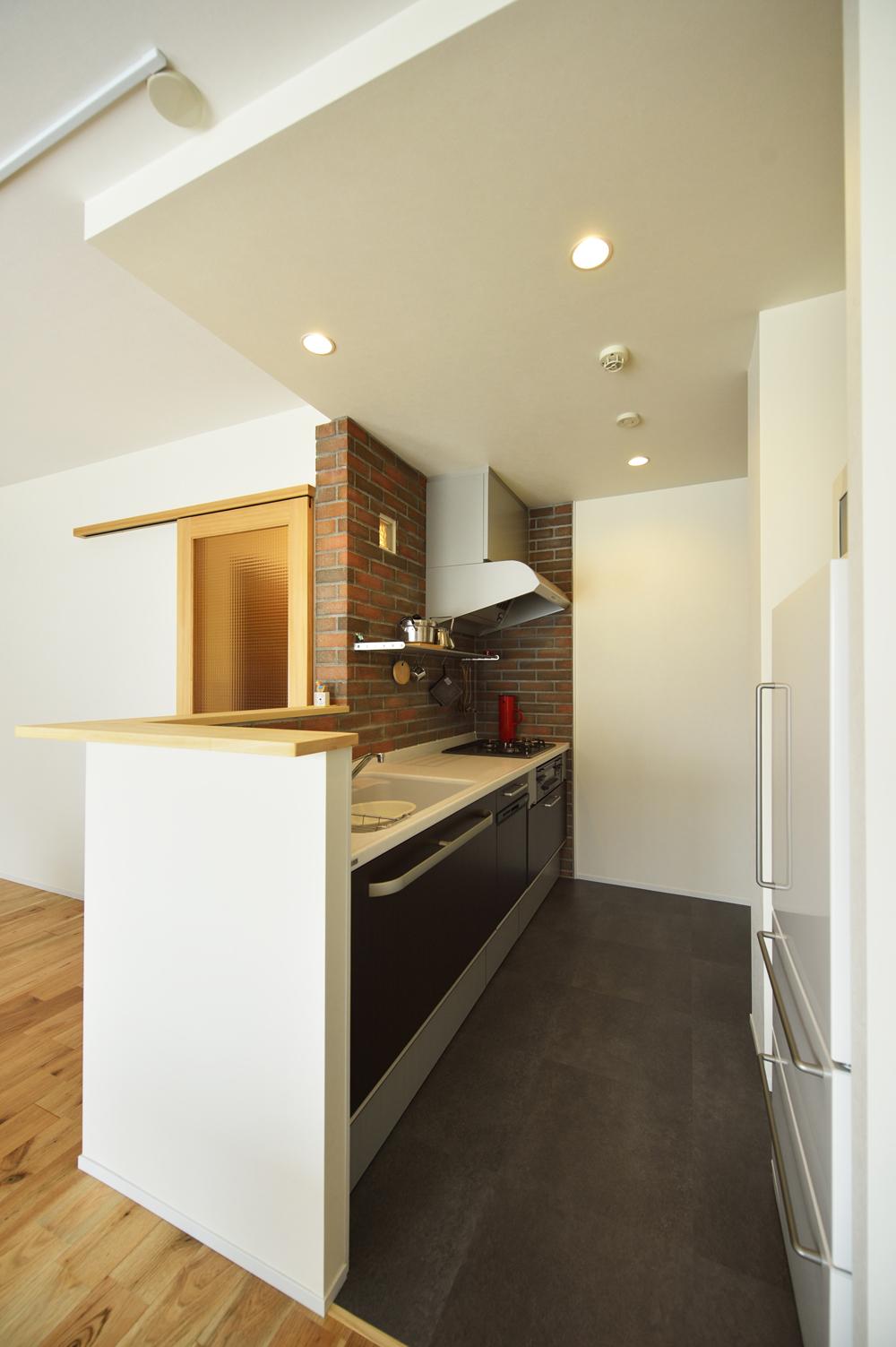 リビング側を向いた対面式のカウンターキッチンに変更しました。壁はレンガ貼りです、そしてガラスブロックを使いたいというご希望もあったので、壁の一部に一つだけガラスブロックを入れています。