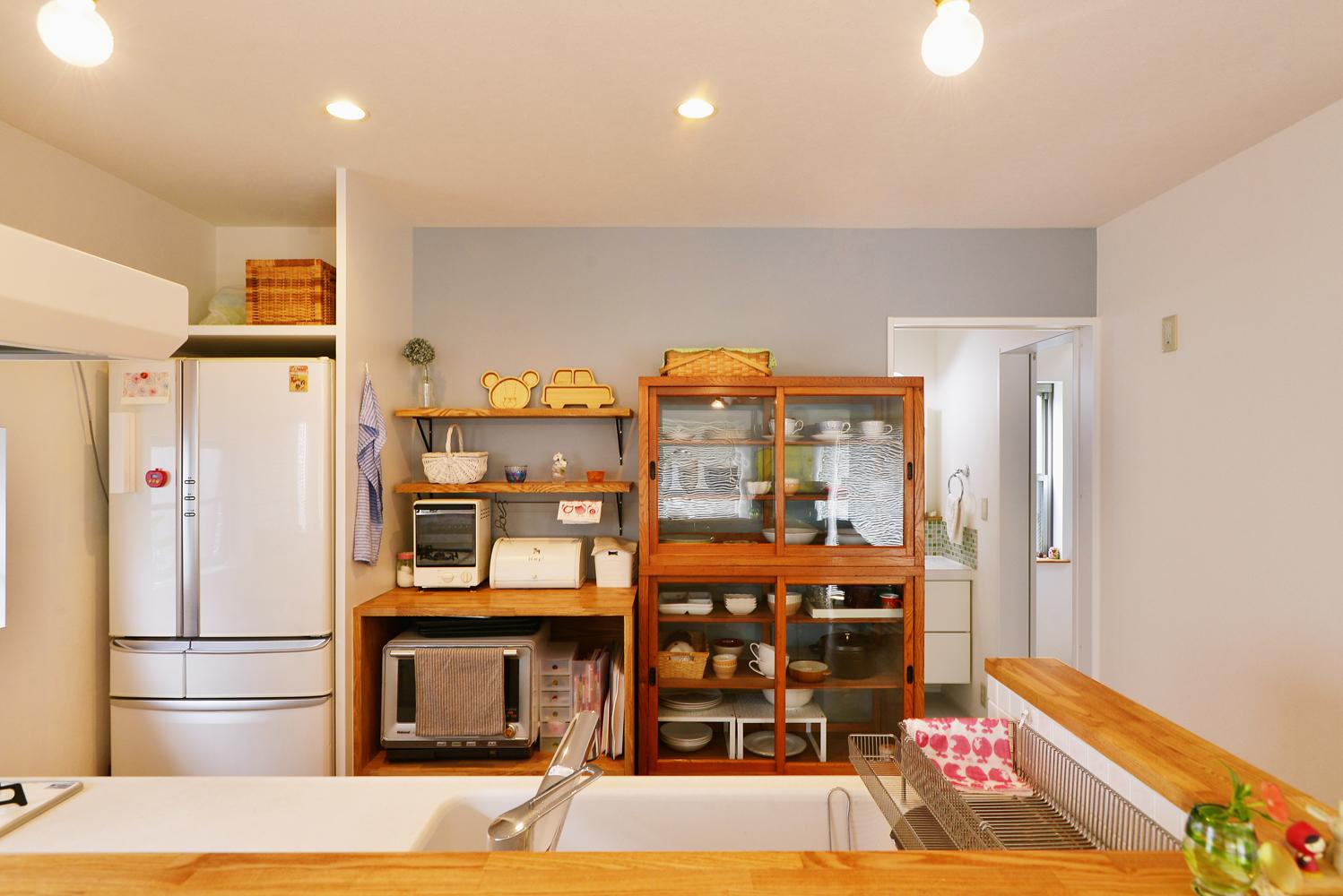 冷蔵庫の隣の家電カウンターは造作しました。その隣の食器棚はお客様が購入したものです。背面の壁が見えるので、この面のみアクセントクロスを使って、食器棚を通してブルーの色が見えるように工夫しました。