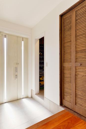 玄関は土間を白いタイル、壁も白のクロスに変えて明るいイメージに一新。隣のリビングの収納スペースを玄関側から使えるようにして、大容量のシュークロークと玄関クロゼットに。