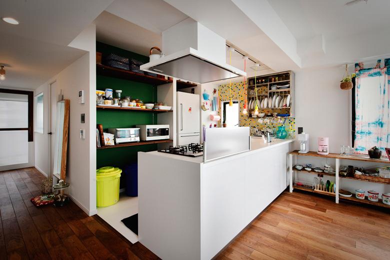 壁を向いていたキッチンは対面式のカウンターキッチンに。背面の収納スペースは、Uさんお気に入りの洋書のイメージを参考に、濃いグリーンの壁にこげ茶の棚を組み合わせました。窓側の壁はグリーンを取り入れたタイル貼り。壁にかかっている食器用のラックはUさんが取り寄せたこだわりのアイテムです。