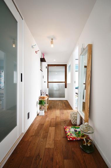 光が入らず、暗くて細長かった廊下は、右側の寝室スペースを少し狭くすることで廊下の横幅を確保。お気に入りの雑貨や身仕度のための鏡も用意し、生活空間として活用。玄関ホールとは大きなガラス戸で仕切り、光が入るようにしました。建具は下部３分の１を白く、残りは木の色で塗装して、軽やかな印象に。