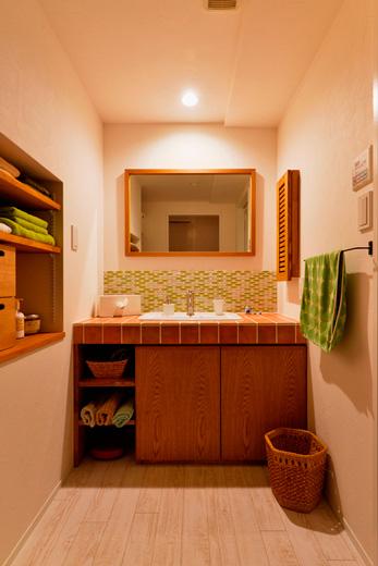 洗面カウンターは造作。カウンターと壁のタイルは、色や大きさなどMさんが選んだもの。壁には歯ブラシを見せずにきちんと収納できる扉付きのニッチを設けています。左側の壁に組み込まれた収納は入れ子状になっており、上部と下部の空間はキッチン側の収納として使っています。