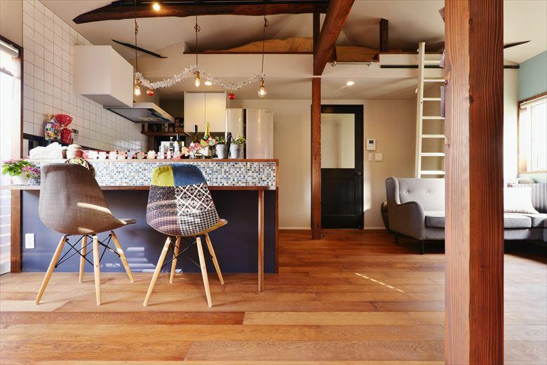 2階の洋室と和室の間仕切りをなくして広々としたＬＤＫに。天井を上げて、より開放感を演出した。小屋裏のスペースは収納用のロフトを設け、Tさんご夫妻の仕事用の書類などもすっきり収納できるように。キッチンカウンターは上部はタイル貼り、下部は濃いブルーのメラミン材。リビングのドアは木製ドアを濃いブルーで塗装