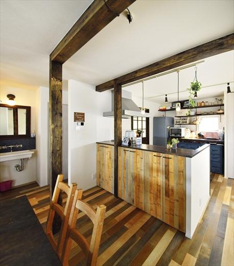 造作のカウンター。ダイニング側の収納棚は、お子さんが触らないように扉を設けた。扉は床材の雰囲気に合わせ、オーク材を２色に塗り分けている。もともと和室だったため、間仕切りをなくした部分は梁で補強。柱と梁はKさんが塗装した。キッチン奥の扉からは廊下と玄関につながる