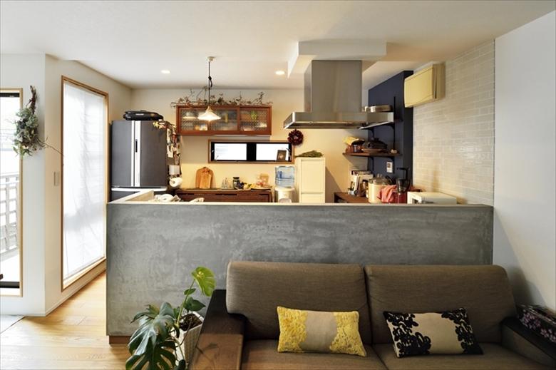 白いタイル貼りの床に白い家具で統一されていた2階リビングは、内装の素材を一新。床は、床暖房に対応したオーク三層無垢材。壁付けのキッチンは向きを変えて対面式に。収納も既存の白い収納棚を撤去して、木製の造作棚に変更した。キッチンのカウンターはモルタル仕上げ。