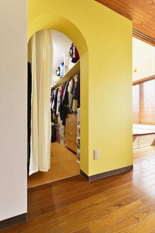 リビングから直接出入りできるウォークインクロゼット。箱のような形とアーチの入口がリビングのアクセントに。壁のクロスは、夫婦ともに一番好きな黄色を取り入れた。内部は枕棚とハンガーパイプのみ取り付け、あとは必要に応じて自由に使うことができる。床はコルクタイル。
