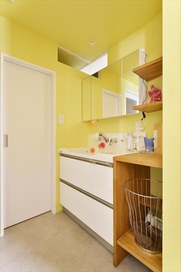洗面室とトイレは窓のない奥まった位置にあるため、天井近くの壁には明かり取りのＦＩＸ窓を。壁は明るい黄緑色のクロスを採用。洗面台の隣の空間には、洗剤や買い置き品、脱衣かごなどをおける棚を造作。扉のないオープンなデザインで使いやすく