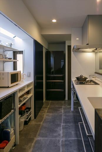 料理をしながらリビングを見渡せる対面キッチン。背面の収納は、既存の出窓を利用した家電収納。ブルーが入った黒の引戸を閉めると内部が見えず、すっきりとした印象に。写真正面の冷蔵庫の隣はパントリー、洗面カウンターへとつながっている