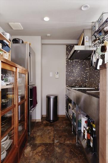 キッチンはステンレスの製品を採用。シンク上の吊り棚もステンレス製。「昔ながらの公団住宅にあるようなもの」というTさんのイメージを叶えた。キッチン周りの壁は、白＋紺＋茶の3色を組み合わせたモザイクタイル貼り。床はフロアタイル