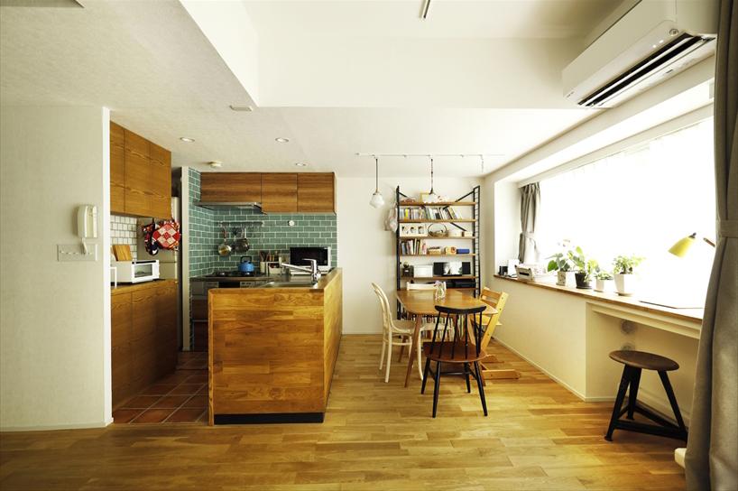 キッチンの上の吊戸棚をなくし、オープンになったダイニングキッチン。窓から入った光がキッチンの奥まで届く。床は90ｍｍ幅のナラ無垢材。窓際のカウンターは既存のもの。天板にタモ材を置くことで温もりのある雰囲気に。エアコン置き場のくぼみの部分はそのまま活かし、デスクとして使えるようにした