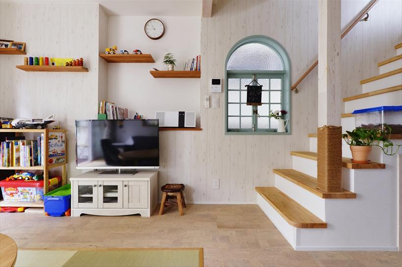 階段の上り口を玄関側からリビング側に変更。以前は階段の影になっていた半円窓を活かしたいというご希望も叶えられ、今では空間の素敵なアクセントになっている。互い違いに配された飾り棚はご主人のアイデアを取り入れたもの