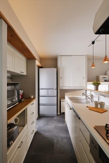 I型の対面キッチンはトクラス。背面のカップボードはIKEAのものを。収納の上にはさらに飾り棚を造作し、間接照明を設置。天井に美しく光が広がる様子を楽しめる。料理をする動線の先に冷蔵庫を置くことで、作業効率もアップ。床は濃いグレーのフロアタイルでシンプルに