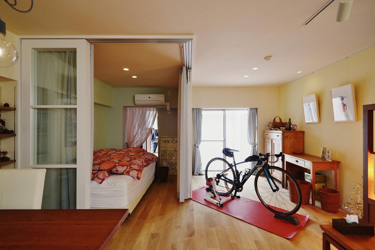 ガラスの框戸＋ルフレブルーのカーテンでゆるく仕切ったベッドスペースは生活の場所と眠る場所は分けつつも、狭く感じないよう工夫しました。