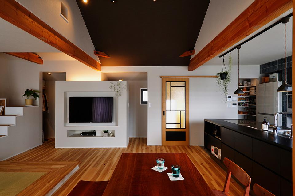 2階は間仕切り壁や収納を撤去し、広々としたＬＤＫに。勾配天井の部分のみ色味を変えることで、落ち着いた大人の空間を演出。リビングドアは造作した。テレビが掛かっている壁の裏側は、リビングで使うものをまとめて隠せる収納。その左隣はご主人の希望を叶えたご主人専用のクロゼット