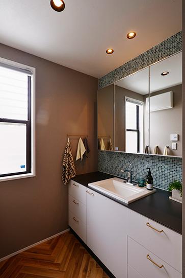 自動水栓の洗面台はオーダーメイド。モノトーンのシンプルなデザインがお洒落。天板が広く、鏡も大きいので、パウダースペースとしても大活躍。壁にあしらったガラスタイルやヘリンボーン柄のフロアタイルは奥さまのセレクト。リゾートホテルのような雰囲気に満ちている