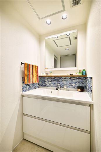 バスルームを広くしたいというご要望から洗面室はコンパクトに。既製の洗面台にブルー系のモザイクタイルをあしらって爽やかな印象に仕上げている。以前は家事室にあった洗濯機置き場も洗面室に移動して洗濯動線が改善された