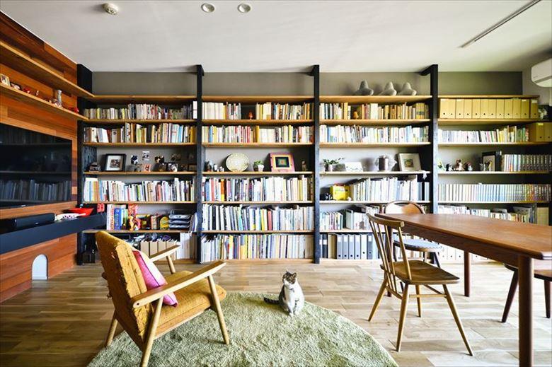 和室を撤去して実現した広々としたリビング。壁面いっぱいにしつらえた書棚が圧巻だ。Kさん自身が手持ちの本やＣＤの量から、必要な書棚の幅を算出したのだそう。テレビは壁掛けを希望され、マホガニー張りの壁は厚みを増して配線などが外に出ないように工夫している。テレビの横には猫用ステップを、下には寝室につながる