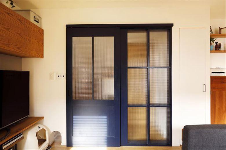 リビングドアは濃紺に。右側の格子部分はＦＩＸ。大判のチェッカーガラスが玄関ホールに光を届けながら、トイレの目隠し役も担っている。ドアの左下が愛猫のスペースになっており、その脇に通り抜けできる開口もしつらえた