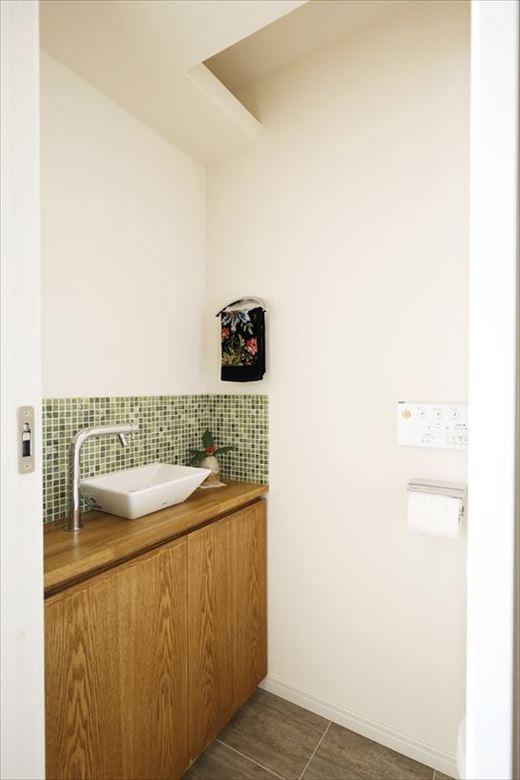 トイレは位置をずらし、洗面室から切り離して独立させたことでアクセスが良くなった。手洗い場にあしらったモザイクタイルも大理石。グリーン系のグラデーションが大人のお洒落感を演出している。反対側の壁には調湿や消臭といった機能面を考慮してエコカラットを採用した