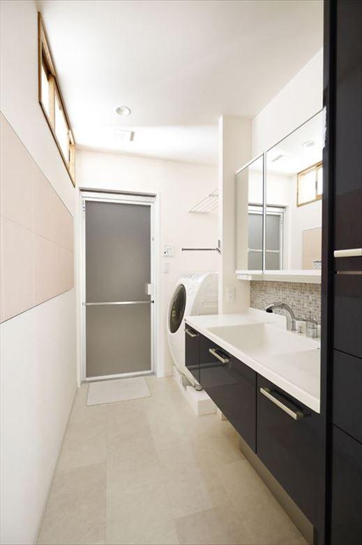 洗面室は水廻りの再配置で位置も広さも変更。住まいの中心に位置しているため、以前は暗くなりがちだったが、主寝室との仕切り壁の高い位置に室内窓を取り付けたことで明るい空間となった。洗面台側にはグレーのモザイクタイルの大理石、背面にはエコカラットをあしらい、上品な雰囲気を添えている