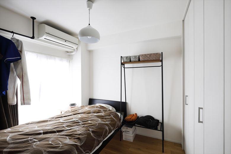 ダブルベッドが入る広さを確保した寝室は白をベースに明るい雰囲気。アイアンの洋服掛けや飾り棚がお洒落に映える。既存の収納を撤去したため、新たに壁面いっぱいに収納を新設。布団やスーツケースが入れられるよう、奥行きもたっぷりと取っている