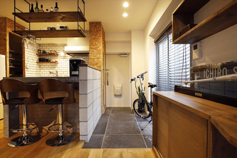 玄関の土間は自転車やゴルフバッグが置けるように拡大。衛生面を考慮してバーカウンターと接する部分には腰壁を新たに設けている。腰壁にはコンクリートブロック調のタイルを採用。モルタル調の大判フロアタイルとともに男っぽい素材感を活かしている