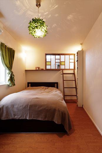 以前は子ども部屋として使われていたらしい1.5階の居室を主寝室に。既存のロフトを撤去してベッドヘッドを造作。その際に不要になったハシゴをインテリアとして再利用。新設した室内窓にはカラーガラスを使ってステンドグラスのような雰囲気に