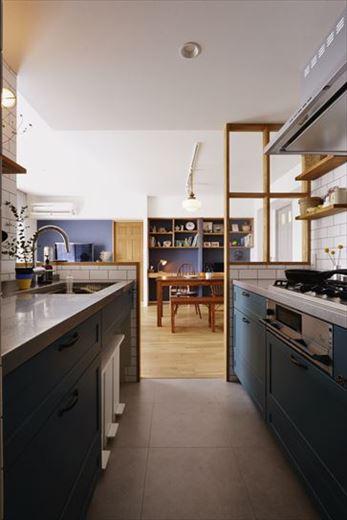 キッチンは省スペースなII型の採用で、できるだけLDに飛び出さないように工夫した。木製キッチンをアクセントクロスにも用いたブルーに塗装。取り込んだ子ども室の開口を活かして水廻り動線を確保している。家電置き場やパントリーの新設で生活感を見せないキッチンに