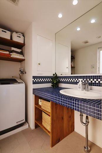 造作の洗面台はタイル貼りでお洒落に仕上げた。立ち上がりはホワイトとブルーのタイルを組み合わせた複数のデザインパターンを提案し、その中から選んだもの。収納部や洗濯機上の棚は濃い目の塗装で統一。大判の鏡が空間の広がりを感じさせる