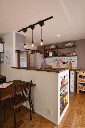 対面キッチンには腰壁を設け、古材風のカウンターを設置。背面の黒アイアン×木の吊り棚や裸電球風の照明などで男前な雰囲気を演出している。右手奥のタイル貼りされていない壁は抜くことができ、将来の家族構成や暮らし方の変化に伴うリノベーションまで考慮した