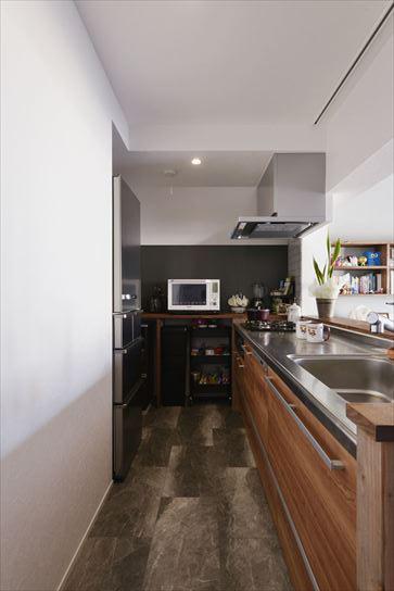 木調をセレクトしたオープンな対面キッチンからダイニングやリビングで寛ぐ家族が見守れ、廊下の先まで見通せる。フロアタイルや側面の壁には黒を使ってシックな印象に仕上げた