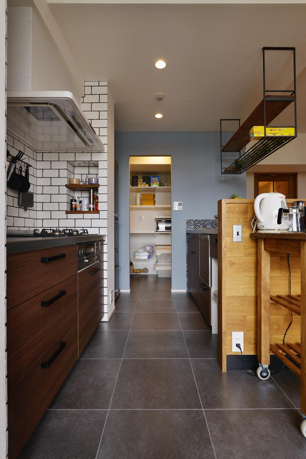 キッチンはリビングに向けて対面にしたセパレートタイプ。壁側は白いシンプルなタイルを、カウンターの裏側は細かなブルーのタイルと使い分けている。奥はパントリー。あまり作りこまず、収納するものに合わせてラックやフックなどを自由に取り付けられるようにした