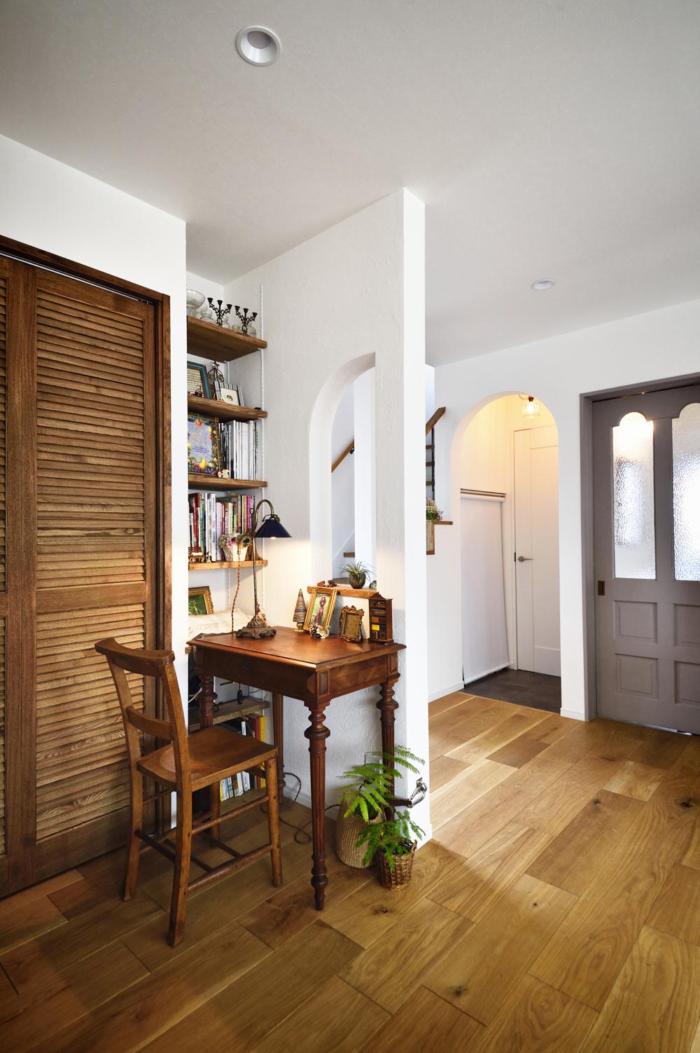 リビングの一角には、夫人の書斎スペースを。構造上抜けない壁は、筋交いの部分をうまく避けながら開口をつくり、視線と光が抜けるように。デスクの横には棚を造作。グレーのドアを開けると玄関ホール。隣のアーチの入口の奥はトイレ。手前の白いロールスクリーンはワンちゃん用のトイレ
