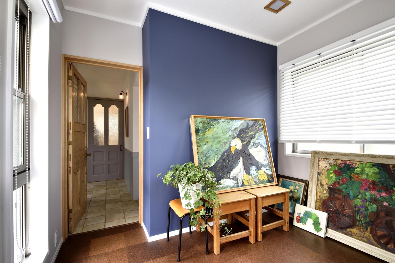 1階の和室は、床をコルクタイルにして洋室に。壁はグレーのクロスで、一面のみブルーのアクセントクロスを。本当は愛犬のケージを置いてプレイルームにする予定だったが、居心地のよさに現在は夫の書斎兼客間として活用しているそう。奥に見える玄関ホールの床は磁器タイル貼り