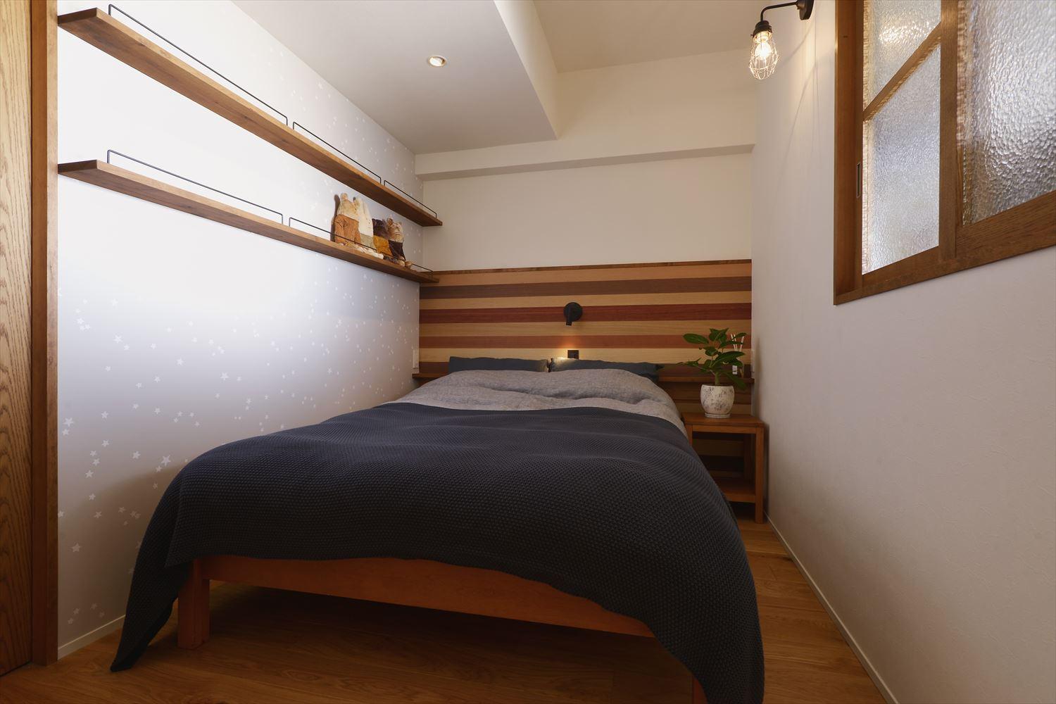 和室の一部を取り込み、大型WICを実現した主寝室。ベッドヘッドにウッドパネルをあしらって落ち着ける雰囲気を演出した。土間スペースとつながる壁に室内窓を取り付け、光と風の通り道を確保している