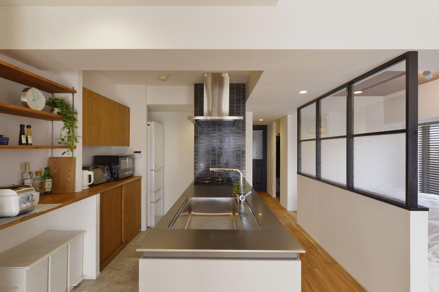 キッチンは向きを変えて無駄のない動線を確保。こだわりのステンレス天板や薄型の換気扇が空間にシャープな印象を与える。背面はオープン棚と隠す収納をうまく使い分けてお洒落な雰囲気に