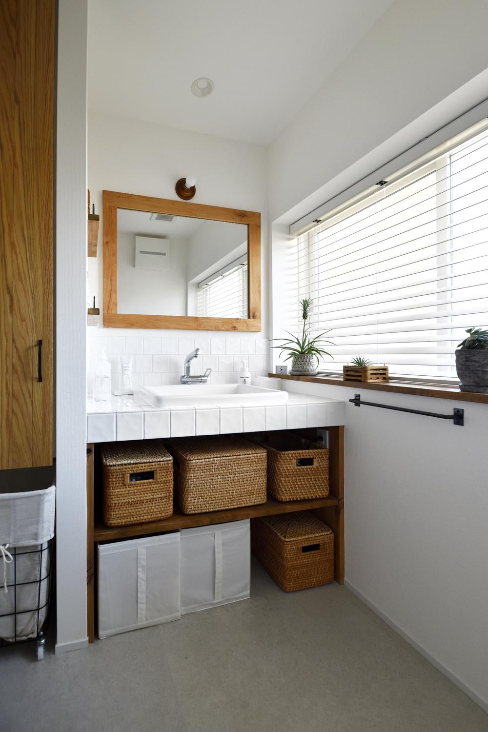 2階の中央に新たに生まれた洗面室。明るい窓際の洗面台は造作。清潔感あるタイル貼りを用い、使いやすいオープン収納に。木製枠の鏡とも爽やかにマッチしている。収納横に配置した洗濯機はキッチンからも近くて便利