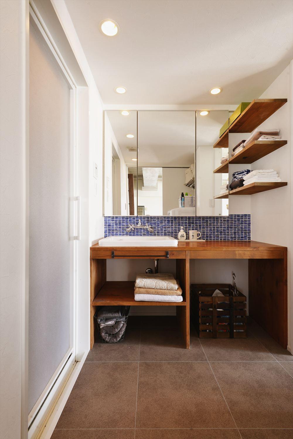 洗面室は出っ張っていた収納を取り払い、ほぼスペースは変わっていないものの広く感じられる。洗面台やオープン棚はシンプルな造作に。ブルーが基調のモザイクタイルが爽やかな印象を与える。浴室や洗面の鏡は既存を利用した