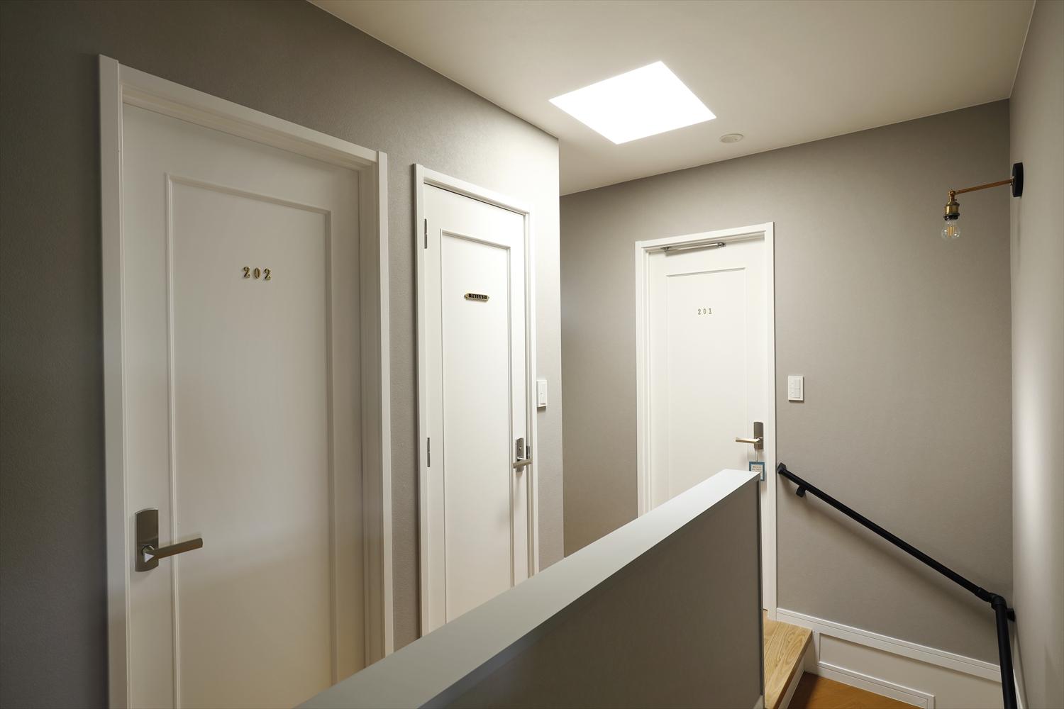 今回、2階はインテリアのみ一新している。建具は既存を白く塗装。ナンバーリングをあしらってホテルの客室をイメージした。壁は淡いグレーを使って落ち着いた雰囲気に。色の濃淡や素材感にこだわり、大き目のサンプルを現地であてながらひとつひとつ吟味した