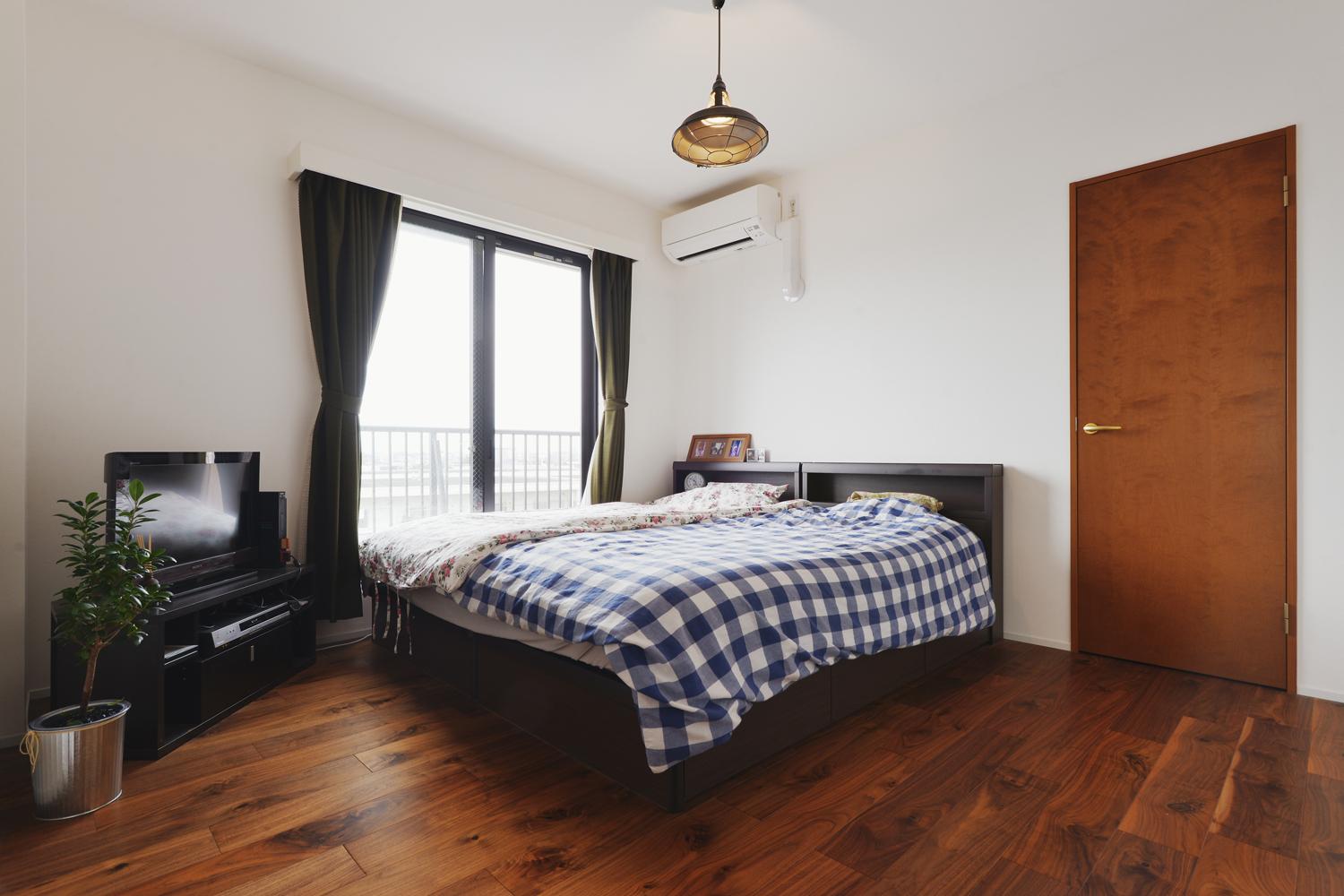 寝室の床はウォールナットの遮音フローリングを採用。住まい全体の木目はこのウォールナットに合わせている。カーテンはダークなオリーブグリーン。ペンダントライトでアンティークな雰囲気を高めて、ゆったりと寛げる空間に