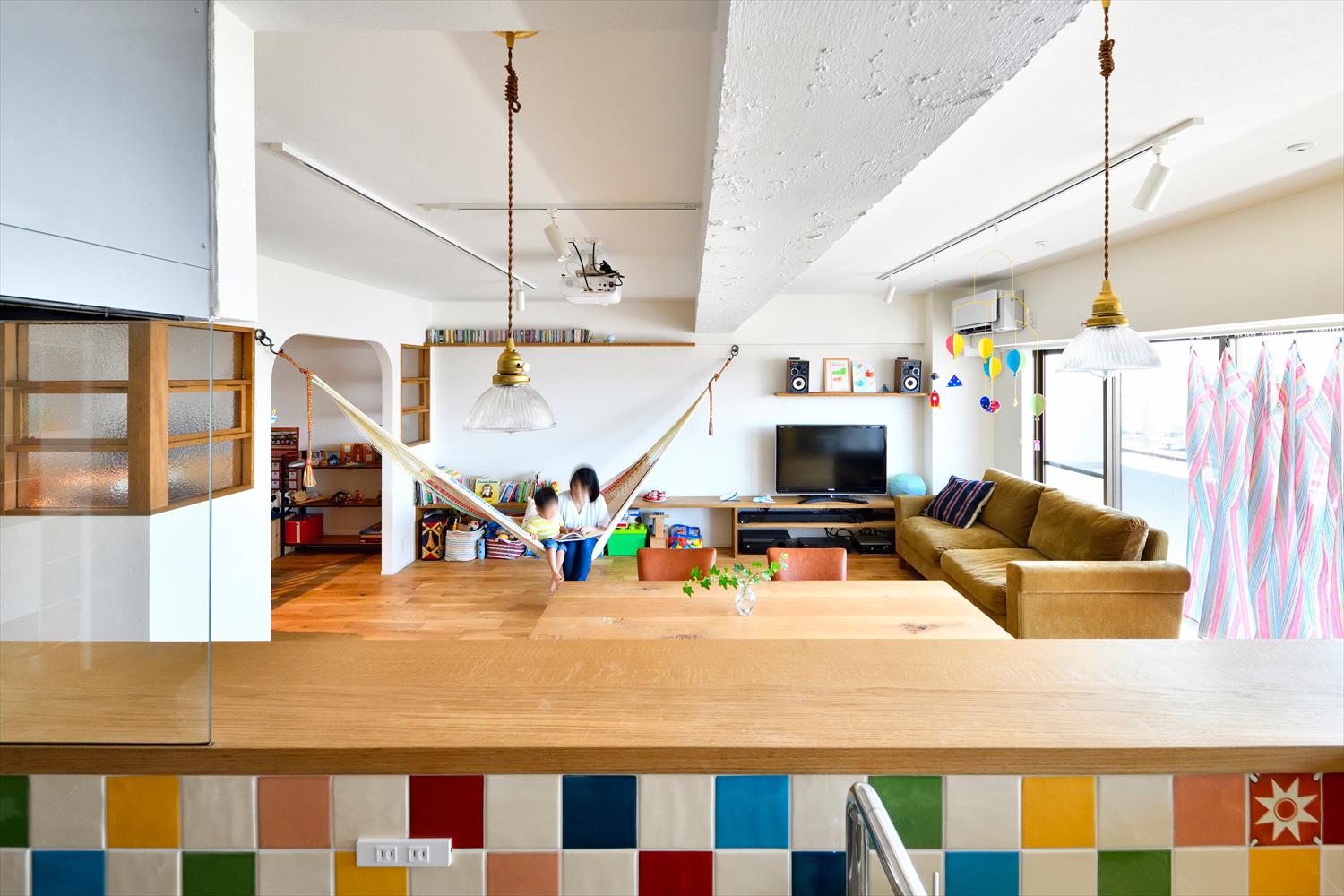 リビングは天井を上げて開放感を高め、現しになった梁にはラフな塗装でナチュラルな雰囲気に。隣接の和室はアール開口のゲストルームとなり、空間の広がりがより感じられるようになった。将来、子ども室として使うときのために開口の両側に室内窓を取り付けている。テレビ横の壁をスクリーンにプロジェクター映像を投影。特