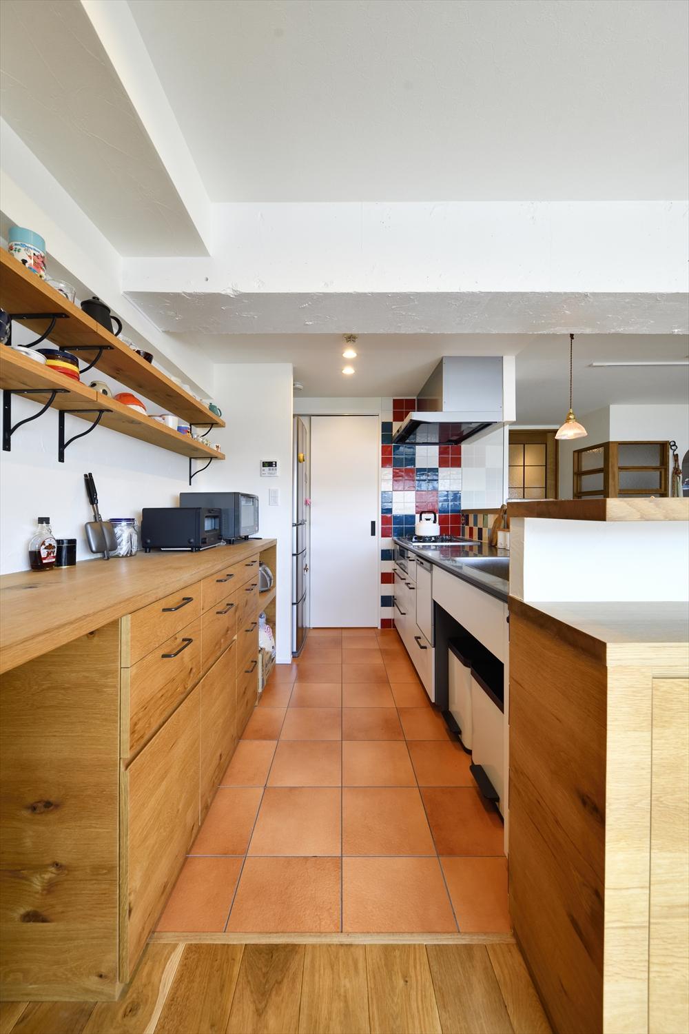 コの字型で閉塞的だったキッチンをフルオープンの対面式に。家族の様子が見守れる。背面は収納とワークスペースを造作し、上部はカフェのような棚を設置した。キッチンの立ち上がりにも収納と飾り棚を設えている。奥の引き戸から洗面室に抜けられ、家事もスムーズ。レンジ脇の壁にあしらったタイルは応援しているサッカーチ