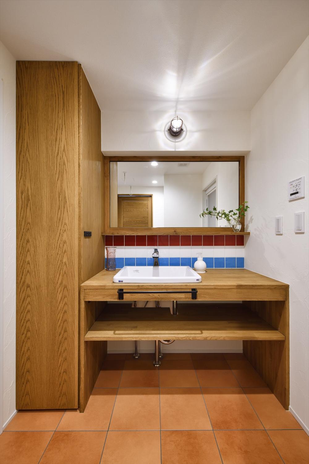 洗面台は造作でシンプルなスタイルに。広めに取ったカウンターはパウダースペース。キッチンと同様にタイルはサッカーチームのカラーを意識してセレクト。床はテラコッタ調、照明はマリンランプ風とディテールにもこだわりが感じられる