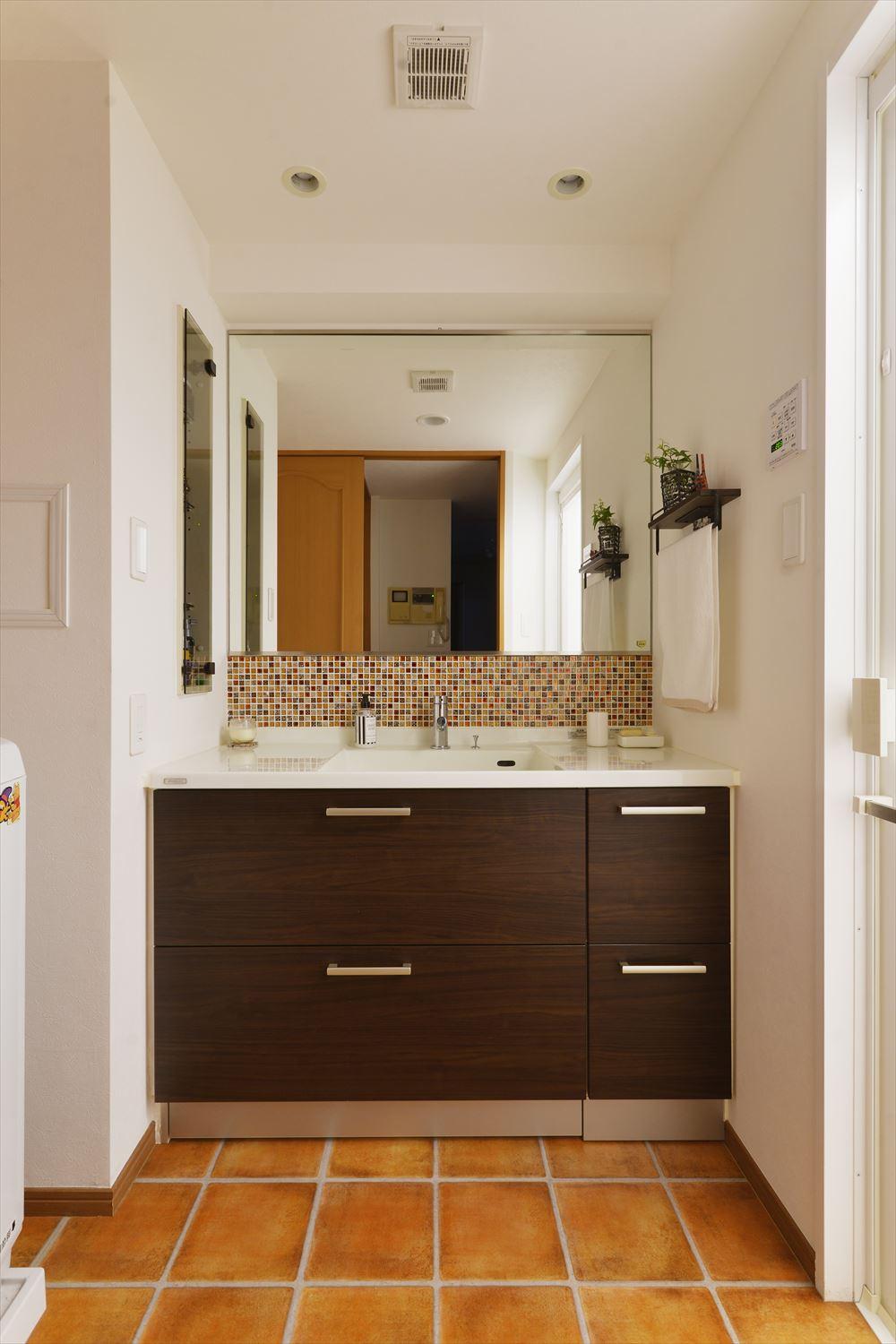 洗面台はLDKと同様にバリ風を意識して焦げ茶の木目の既製品を採用。鏡との間にモザイクタイルをあしらってオリジナリティを演出した。床はキッチンやトイレと同じテラコッタ調にすることで統一感を出している