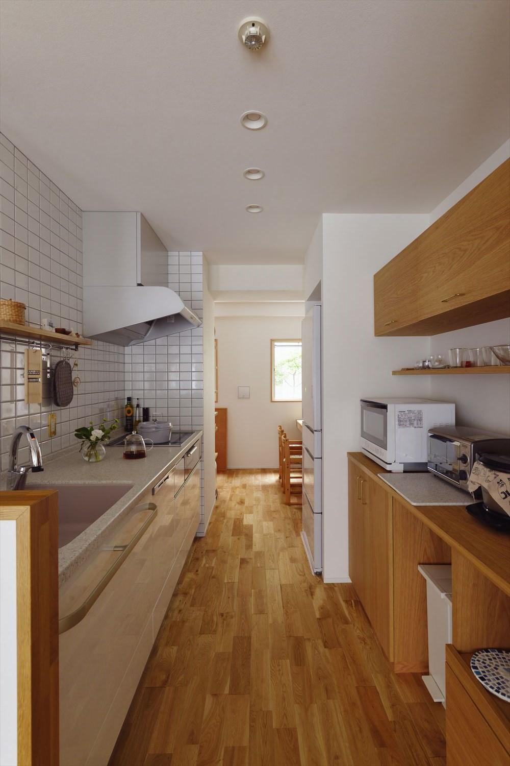 独立型キッチンはLD側へ移動し、家族の様子が見守れるように。壁面は清潔感溢れる真っ白なタイル貼り。造作の背面収納は上下で分け、ダストボックスなどもスッキリと収まる。キッチンだったところはパントリー兼ワークスペースに