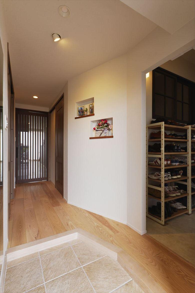 土間はSICに行き来できるよう角を落とした。斜めに設置した居室の壁には奥様が趣味で始めたアーティフィシャルフラワーアレンジメントが飾れるニッチをつくった。玄関ホールの華やかなアクセントになっている