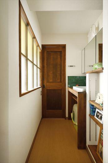 寝室の一部を使って独立した洗面室に。寝室から行き来できる動線は既存を活かしている。下部に猫ちゃんトイレのスペースを確保した洗面台は造作。木の色は濃い目に仕上げ、キッチンと同じタイルをあしらって統一感を出した。室内窓を通して寝室からの光が届き、明るい空間を実現している