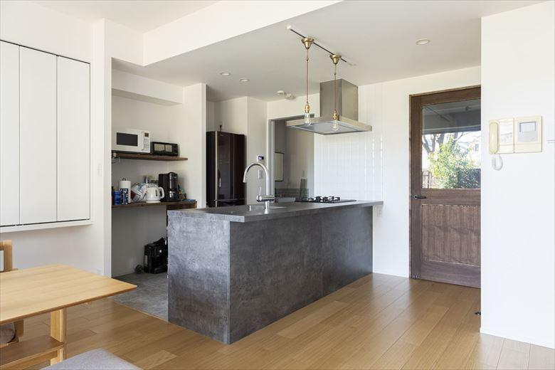 孤立していたキッチンは壁を取って向きを変更。広々と開放的なLDKが実現した。スタイリッシュなグレーのシステムキッチンはフラットカウンターを選び、立ち上がりなどのコストを削減。タイルや、リビングドアなどでＳさん好みのアンティークな雰囲気に