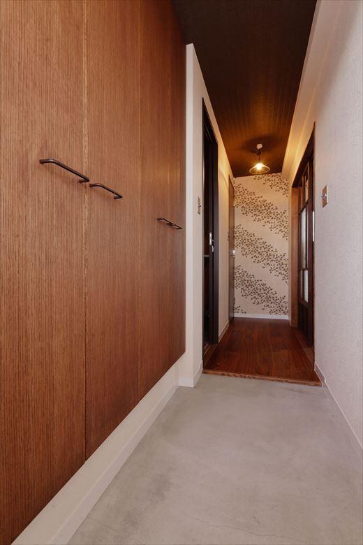 玄関土間はモルタル塗りに。靴収納の内部はそのままに、白かった扉や天井を木目に変更。玄関扉を開けた瞬間のイメージがガラリと変わった。アンティーク調の廊下の照明や廊下突き当りのアクセントクロスが効いている